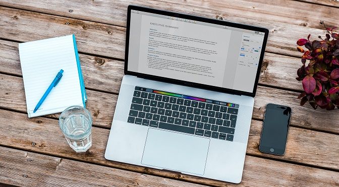 A laptop pen book glass and mobile on a table